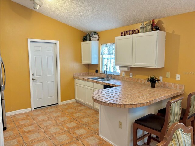 2779 Theresa Dr, Kissimmee, FL 34744 - kitchen featuring a sink, a breakfast bar, a peninsula, white cabinetry, and a textured ceiling