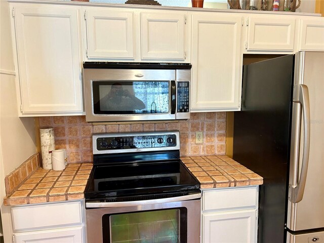 2779 Theresa Dr, Kissimmee, FL 34744 - kitchen featuring stainless steel appliances, tile counters, white cabinets, and backsplash