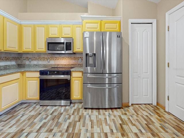 3811 Gator Bay Ln, Saint Cloud, FL 34772 - kitchen featuring appliances with stainless steel finishes, light wood-style flooring, tasteful backsplash, vaulted ceiling, and light stone counters
