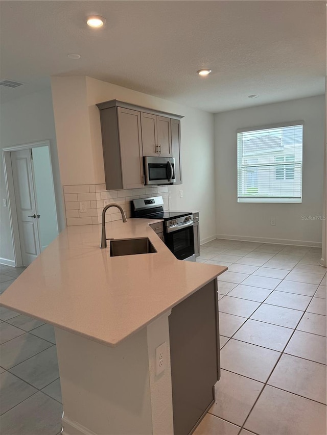 4053 Redbridge Loop, Davenport, FL 33837 - kitchen featuring appliances with stainless steel finishes, a sink, a peninsula, gray cabinetry, and backsplash