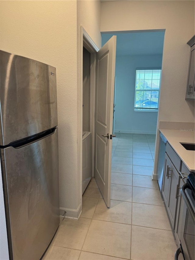 4053 Redbridge Loop, Davenport, FL 33837 - kitchen featuring freestanding refrigerator, washer / clothes dryer, light tile patterned flooring, light countertops, and gray cabinetry