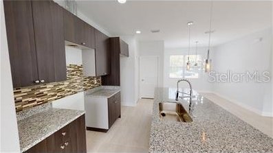 212 Grouper Ct, Poinciana, FL 34759 - kitchen with tasteful backsplash, dark brown cabinets, modern cabinets, light stone counters, and baseboards