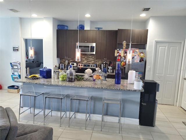 212 Grouper Ct, Poinciana, FL 34759 - kitchen featuring appliances with stainless steel finishes, tasteful backsplash, a kitchen bar, dark brown cabinetry, and light tile patterned floors