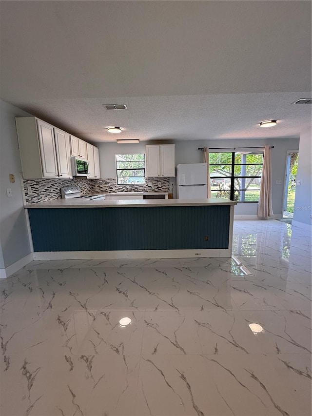 6489 Creation St, Saint Cloud, FL 34771 - kitchen with white appliances, a textured ceiling, a peninsula, backsplash, and white cabinets