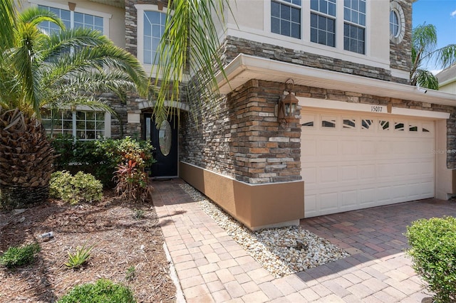 15037 Cedar Branch Way, Orlando, FL 32824 - doorway to property featuring stone siding, a garage, stucco siding, and decorative driveway