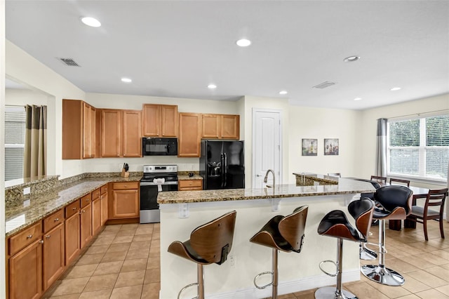 341 Lasso Dr, Kissimmee, FL 34747 - kitchen with black appliances, light stone counters, a breakfast bar, a sink, and light tile patterned flooring