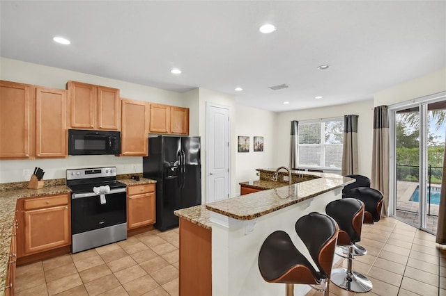 341 Lasso Dr, Kissimmee, FL 34747 - kitchen with black appliances, light tile patterned floors, light stone countertops, a kitchen breakfast bar, and recessed lighting