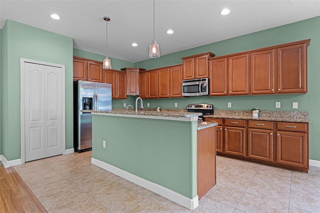 1394 Palmetto Dunes St, Champions Gate, FL 33896 - kitchen with stainless steel appliances, brown cabinetry, hanging light fixtures, an island with sink, and a textured ceiling