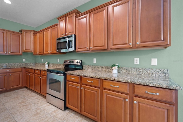 1394 Palmetto Dunes St, Champions Gate, FL 33896 - kitchen featuring stainless steel appliances, brown cabinets, light stone countertops, light tile patterned flooring, and a textured ceiling