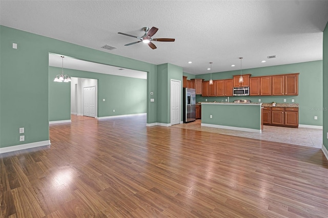 1394 Palmetto Dunes St, Champions Gate, FL 33896 - unfurnished living room with ceiling fan, light wood finished floors, baseboards, a chandelier, and a textured ceiling