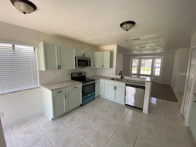 198 N Lake Ct, Kissimmee, FL 34743 - kitchen featuring stainless steel appliances, a sink, a peninsula, baseboards, and a textured ceiling