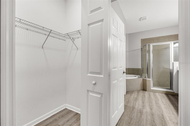 1628 Portofino Meadows Blvd, Orlando, FL 32824 - bathroom with wood finished floors, a garden tub, a stall shower, a spacious closet, and baseboards