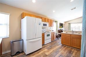 3030 Eagle Crossing Dr, Kissimmee, FL 34746 - kitchen with white appliances, light countertops, wood finished floors, lofted ceiling, and recessed lighting
