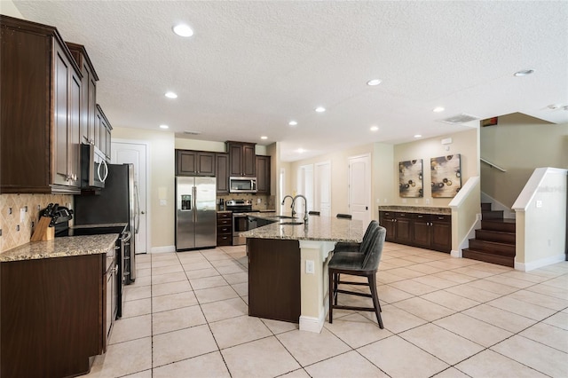 7616 Brookhurst Ln, Kissimmee, FL 34747 - kitchen with appliances with stainless steel finishes, backsplash, a breakfast bar, dark brown cabinets, and a textured ceiling