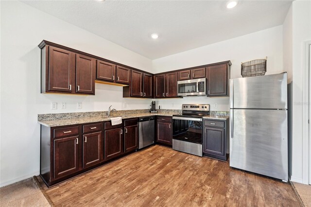 955 Grandin St, Davenport, FL 33837 - kitchen with stainless steel appliances, dark brown cabinetry, wood finished floors, light stone countertops, and a sink