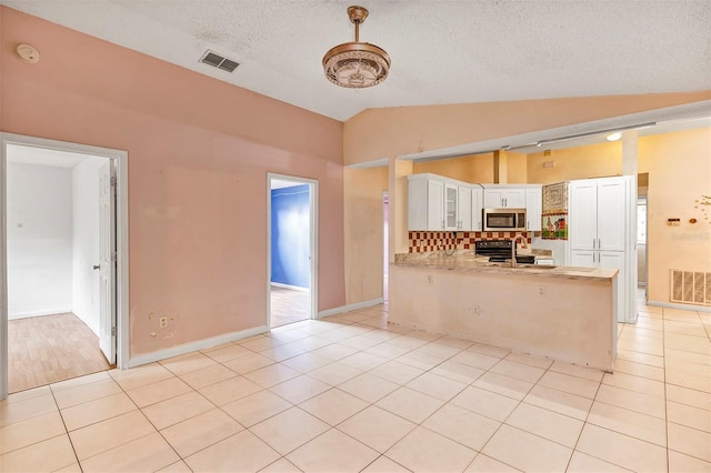 600 Regency Way, Kissimmee, FL 34758 - kitchen with stainless steel microwave, vaulted ceiling, a peninsula, white cabinets, and light countertops