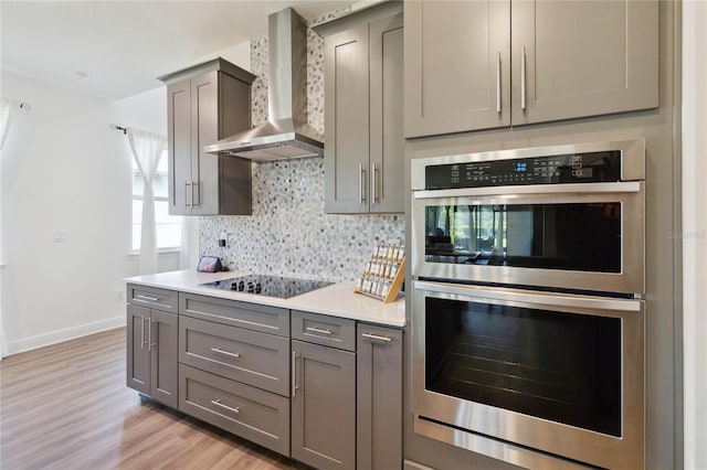 3224 Oxbow Ct, Harmony, FL 34773 - kitchen featuring wall chimney exhaust hood, stainless steel double oven, black electric stovetop, gray cabinetry, and backsplash