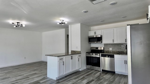 4546 Ontario Dr, New Port Richey, FL 34652 - kitchen with appliances with stainless steel finishes, a peninsula, wood finished floors, white cabinets, and dark stone countertops