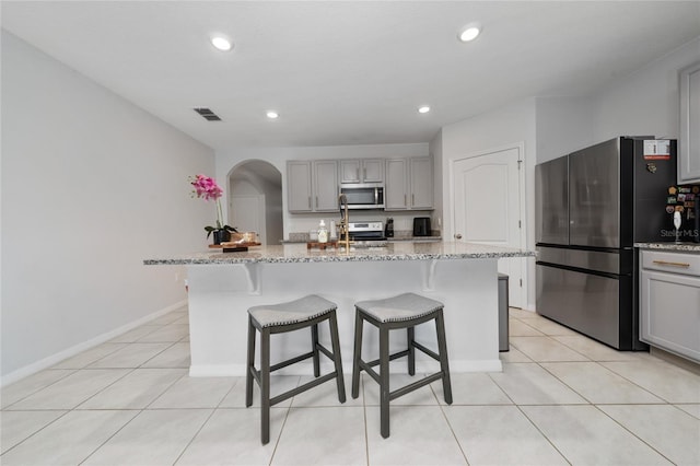 2726 Harmonia Hammock Rd, Harmony, FL 34773 - kitchen featuring gray cabinetry, appliances with stainless steel finishes, arched walkways, a breakfast bar, and light tile patterned flooring