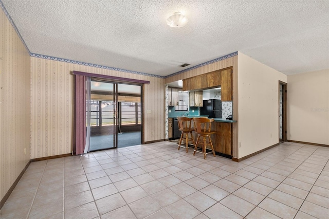 4307 Oak Ct, Saint Cloud, FL 34769 - kitchen with freestanding refrigerator, a textured ceiling, a kitchen breakfast bar, dark countertops, and brown cabinetry