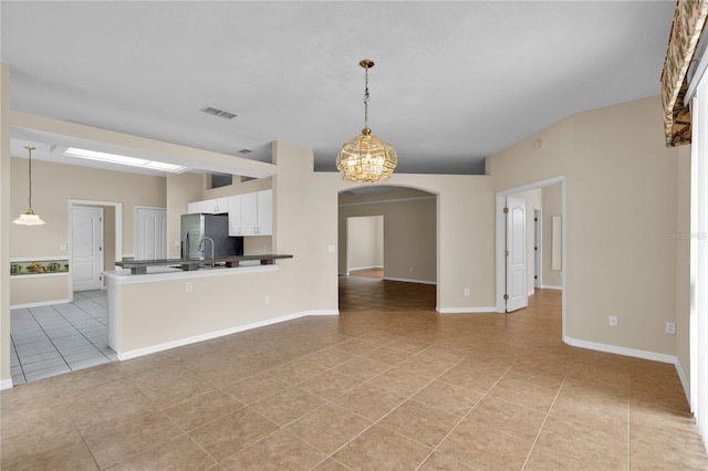 4065 Kingsley St, Clermont, FL 34711 - kitchen with light tile patterned floors, white cabinets, stainless steel fridge, arched walkways, and decorative light fixtures