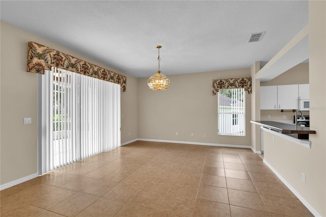 4065 Kingsley St, Clermont, FL 34711 - kitchen with white microwave, white cabinets, a chandelier, light tile patterned floors, and hanging light fixtures