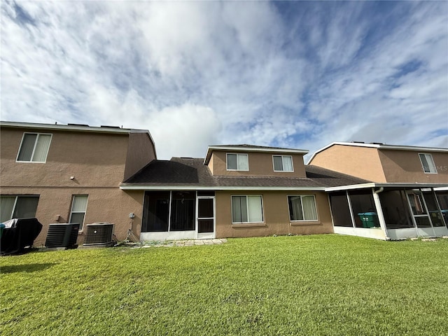 rear view of house featuring a sunroom, a yard, stucco siding, and a shingled roof