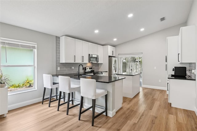 2700 Palm Isle Way, Orlando, FL 32829 - kitchen featuring stainless steel appliances, a peninsula, dark countertops, tasteful backsplash, and light wood-style floors