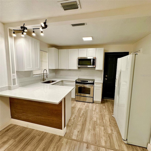 1615 NE 9th St, Ocala, FL 34470 - kitchen with appliances with stainless steel finishes, a sink, a peninsula, white cabinetry, and light wood-style flooring