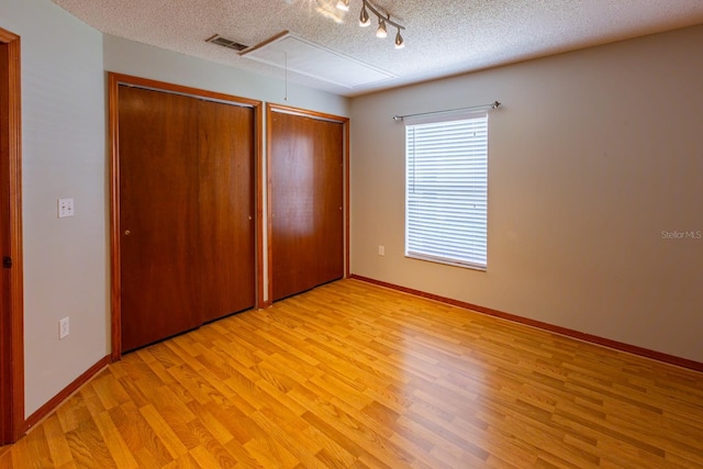 3267 Villa Way Cir, Saint Cloud, FL 34769 - unfurnished bedroom with attic access, light wood-style floors, multiple closets, track lighting, and a textured ceiling