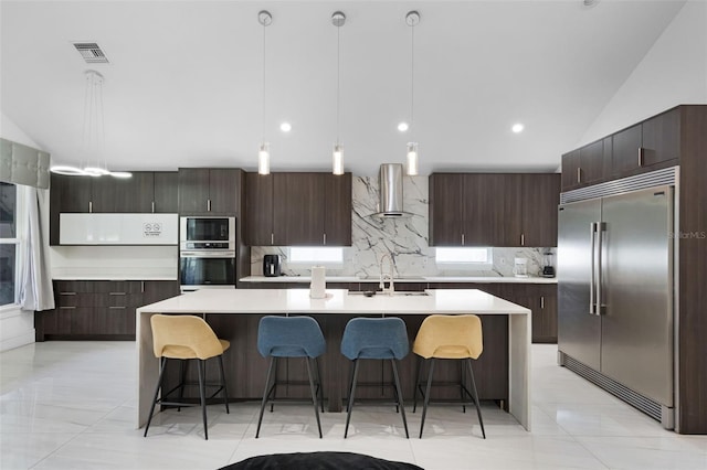 2561 Montego Bay Blvd, Kissimmee, FL 34746 - kitchen with built in appliances, wall chimney exhaust hood, tasteful backsplash, dark brown cabinetry, and a spacious island
