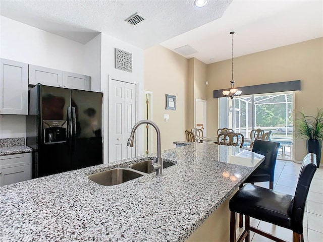 116 Westport Ln, Davenport, FL 33896 - kitchen with black fridge, a sink, a breakfast bar, light stone counters, and hanging light fixtures