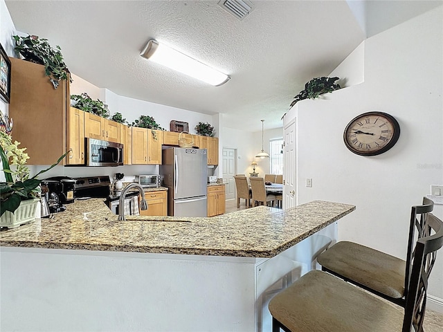 107 Amaca Ln, Davenport, FL 33897 - kitchen with stainless steel appliances, a peninsula, a textured ceiling, a kitchen bar, and light stone countertops