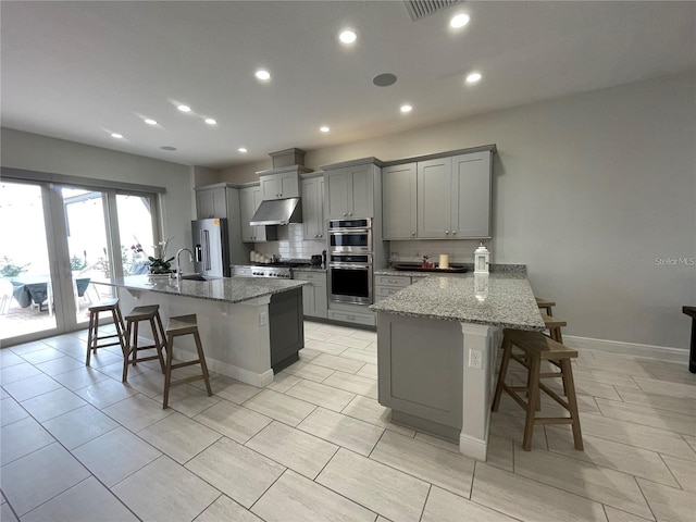 8919 Lakeshore Pointe Dr, Winter Garden, FL 34787 - kitchen featuring appliances with stainless steel finishes, gray cabinets, a kitchen bar, under cabinet range hood, and recessed lighting