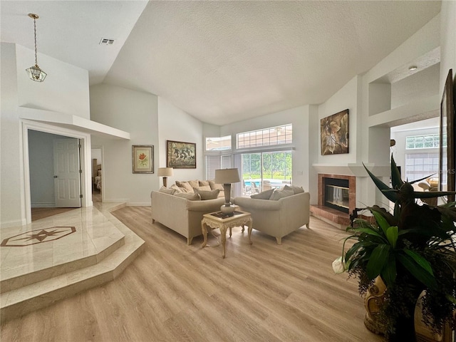 2356 Chadwick Cir, Kissimmee, FL 34746 - living room with a tiled fireplace, light wood finished floors, a textured ceiling, baseboards, and high vaulted ceiling