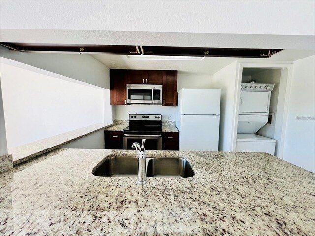 658 Caribbean Dr, Davenport, FL 33897 - kitchen featuring appliances with stainless steel finishes, stacked washer / dryer, dark brown cabinets, light stone counters, and a sink
