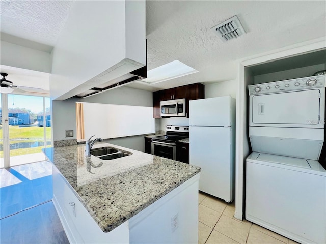 658 Caribbean Dr, Davenport, FL 33897 - kitchen featuring appliances with stainless steel finishes, a sink, stacked washer / dryer, a textured ceiling, and a peninsula