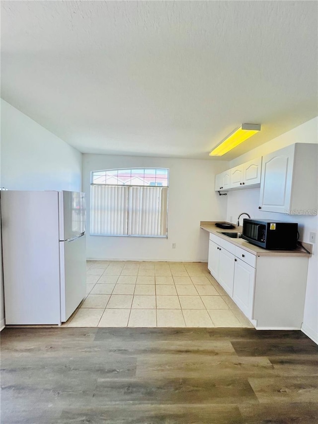 658 Caribbean Dr, Davenport, FL 33897 - kitchen featuring freestanding refrigerator, black microwave, white cabinets, light wood finished floors, and a sink