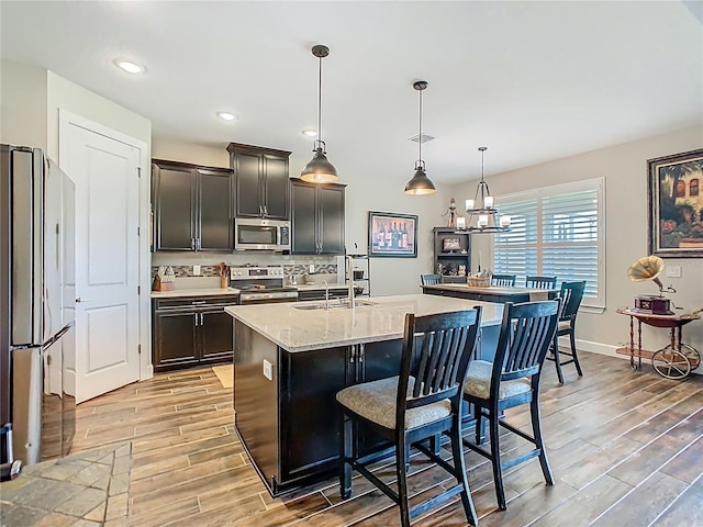 605 San Augusto Dr, Kissimmee, FL 34759 - kitchen featuring appliances with stainless steel finishes, light wood-style floors, an island with sink, a kitchen bar, and decorative light fixtures