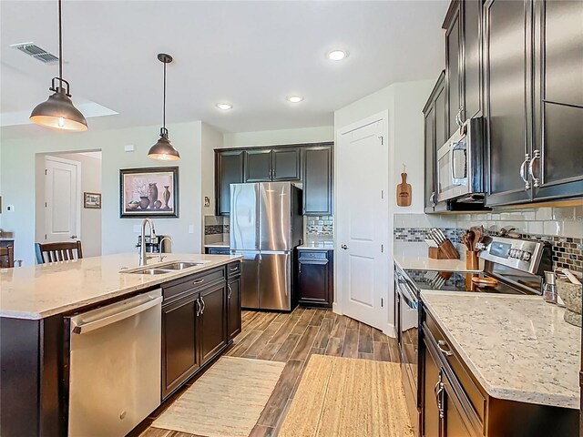 605 San Augusto Dr, Kissimmee, FL 34759 - kitchen featuring appliances with stainless steel finishes, a center island with sink, dark wood finished floors, tasteful backsplash, and pendant lighting