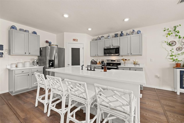 176 Sofia Ln, Lake Alfred, FL 33850 - kitchen with stainless steel appliances, dark wood-style flooring, a breakfast bar, light countertops, and a center island with sink