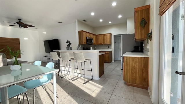 3901 Ballinore Pl, Gotha, FL 34734 - kitchen featuring stainless steel microwave, brown cabinetry, ceiling fan, a peninsula, and light countertops