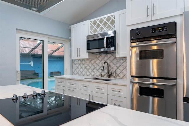 5015 Nassau Cir Unit 4, Orlando, FL 32808 - kitchen featuring appliances with stainless steel finishes, a sink, decorative backsplash, white cabinetry, and lofted ceiling