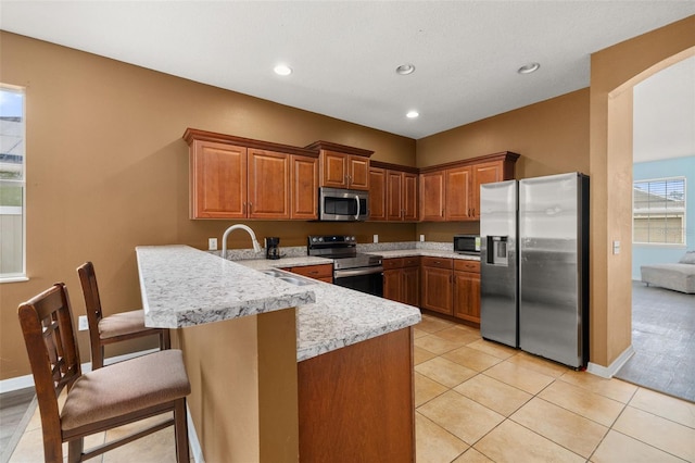 326 Highland Meadows Ave, Davenport, FL 33837 - kitchen with appliances with stainless steel finishes, a peninsula, a kitchen breakfast bar, brown cabinetry, and a sink