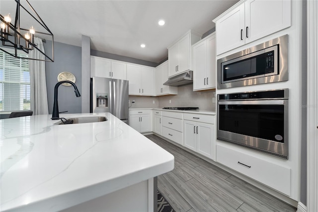1335 Greenfield Loop, Kissimmee, FL 34747 - kitchen with stainless steel appliances, a sink, a chandelier, light wood-style flooring, and white cabinets