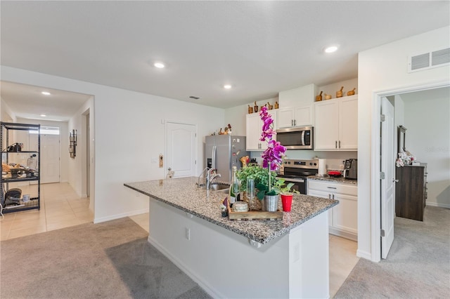 1102 Tupelo Trl, Haines City, FL 33844 - kitchen with stainless steel appliances, light carpet, white cabinetry, a center island with sink, and light stone counters