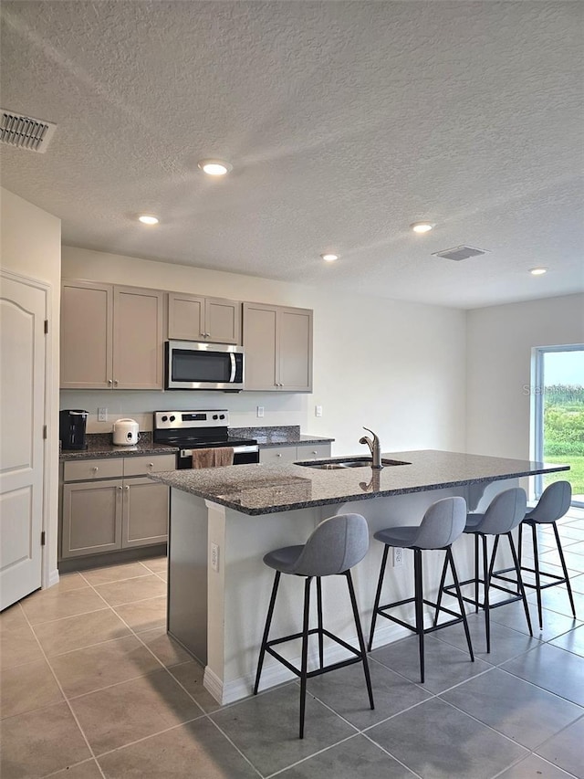 3886 Whitney Way, Haines City, FL 33844 - kitchen with appliances with stainless steel finishes, gray cabinetry, a kitchen bar, light tile patterned flooring, and a textured ceiling