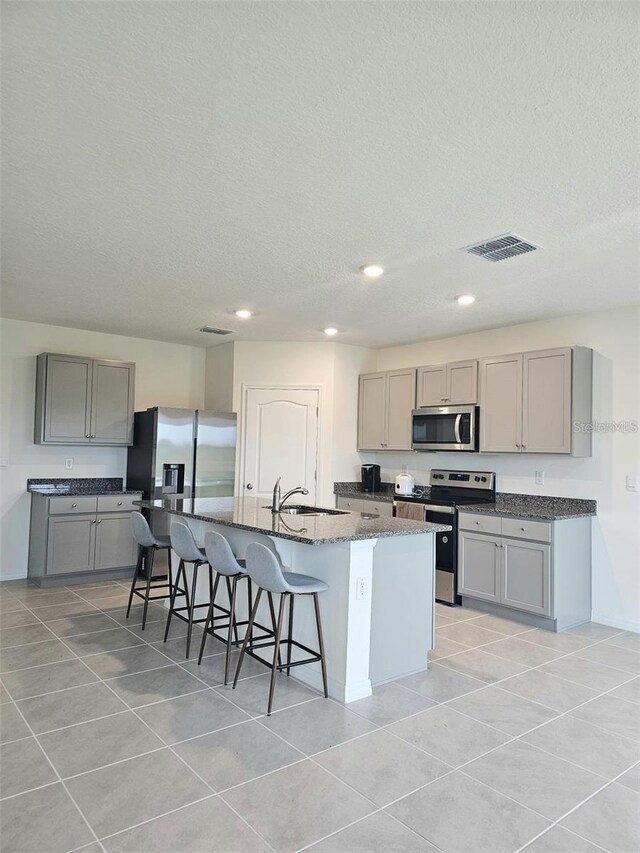 3886 Whitney Way, Haines City, FL 33844 - kitchen with gray cabinets, stainless steel appliances, an island with sink, a breakfast bar area, and light tile patterned floors