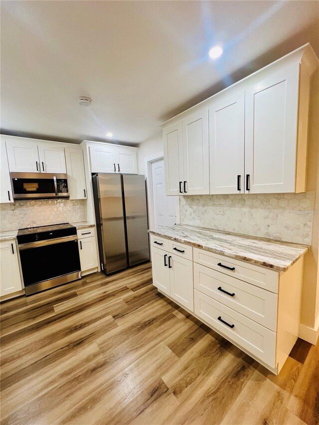 801 Leeward Way, Palm Harbor, FL 34685 - kitchen featuring appliances with stainless steel finishes, tasteful backsplash, light wood finished floors, white cabinets, and light stone countertops