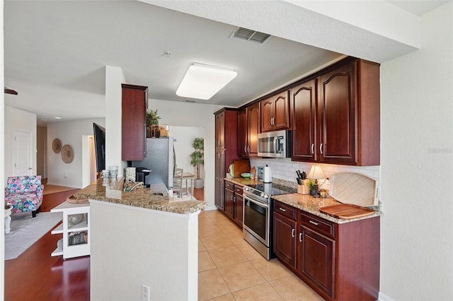1225 Bella Cara Ct Unit 1, Davenport, FL 33896 - kitchen featuring appliances with stainless steel finishes, tasteful backsplash, light stone countertops, a peninsula, and light tile patterned floors